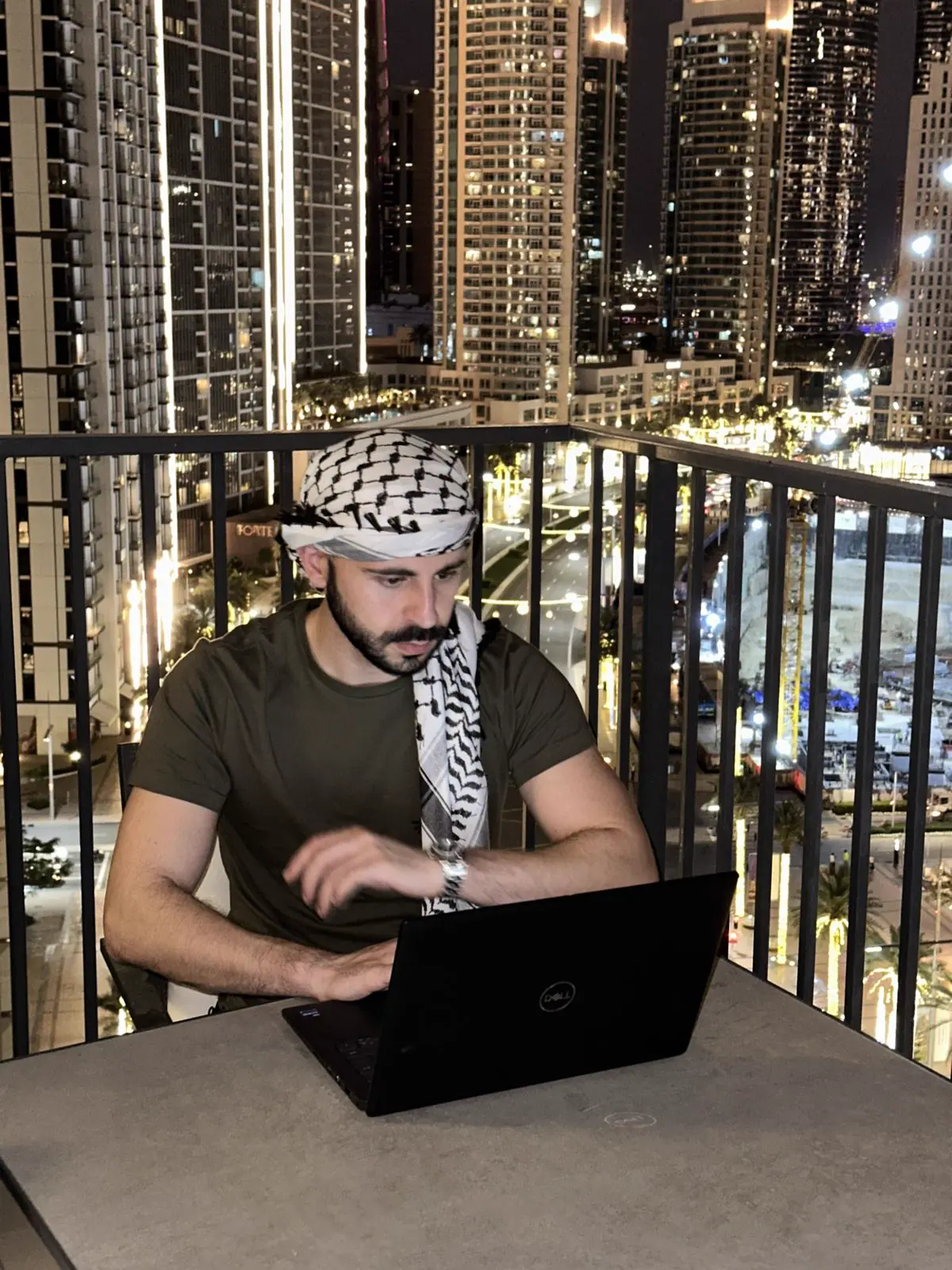Korak Taher working on his laptop at night on a balcony overlooking the Dubai skyline